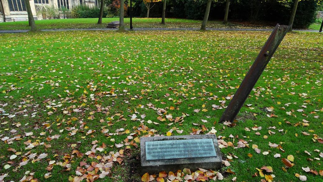 A length of iron tram rail sticking out of the grass in the churchyard, with a small plaque