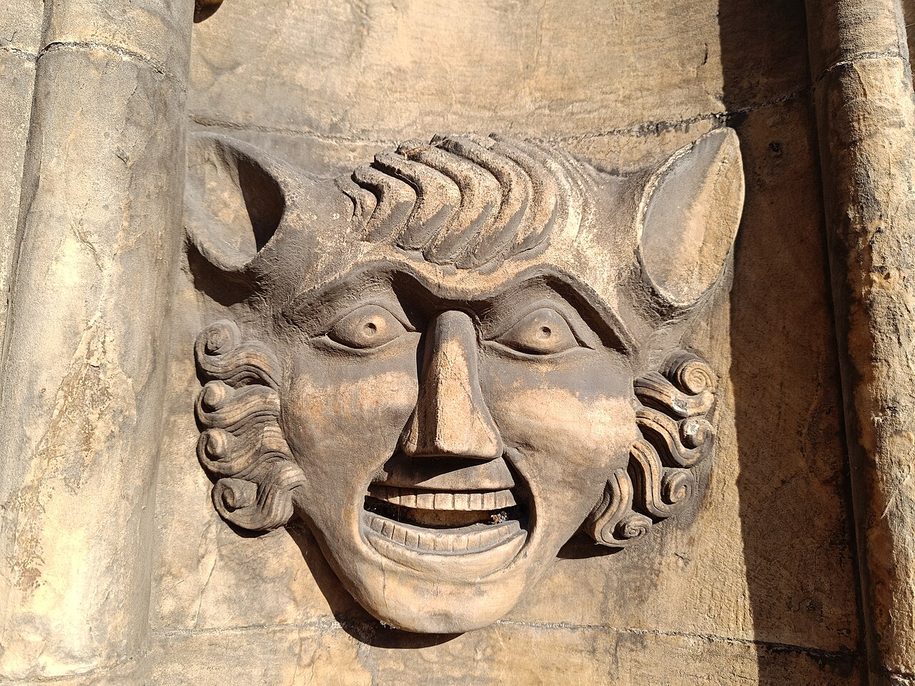 A carved stone head with a broad grin and horn-like ears on a wall inside St Mary's, Beverley