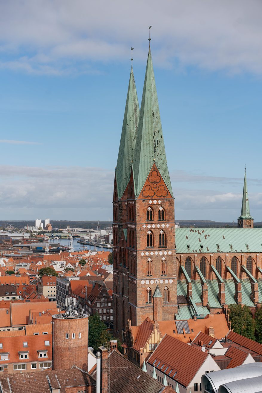 Aerial view of St Mary's Church in Lübeck, a huge red-brick Gothic church with twin green copper spires, above the old town roofs