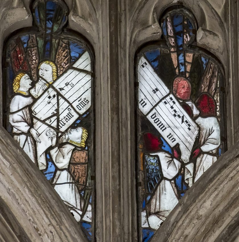 Medieval stained glass in the tracery of the Beauchamp Chapel windows, showing angels holding scrolls of music