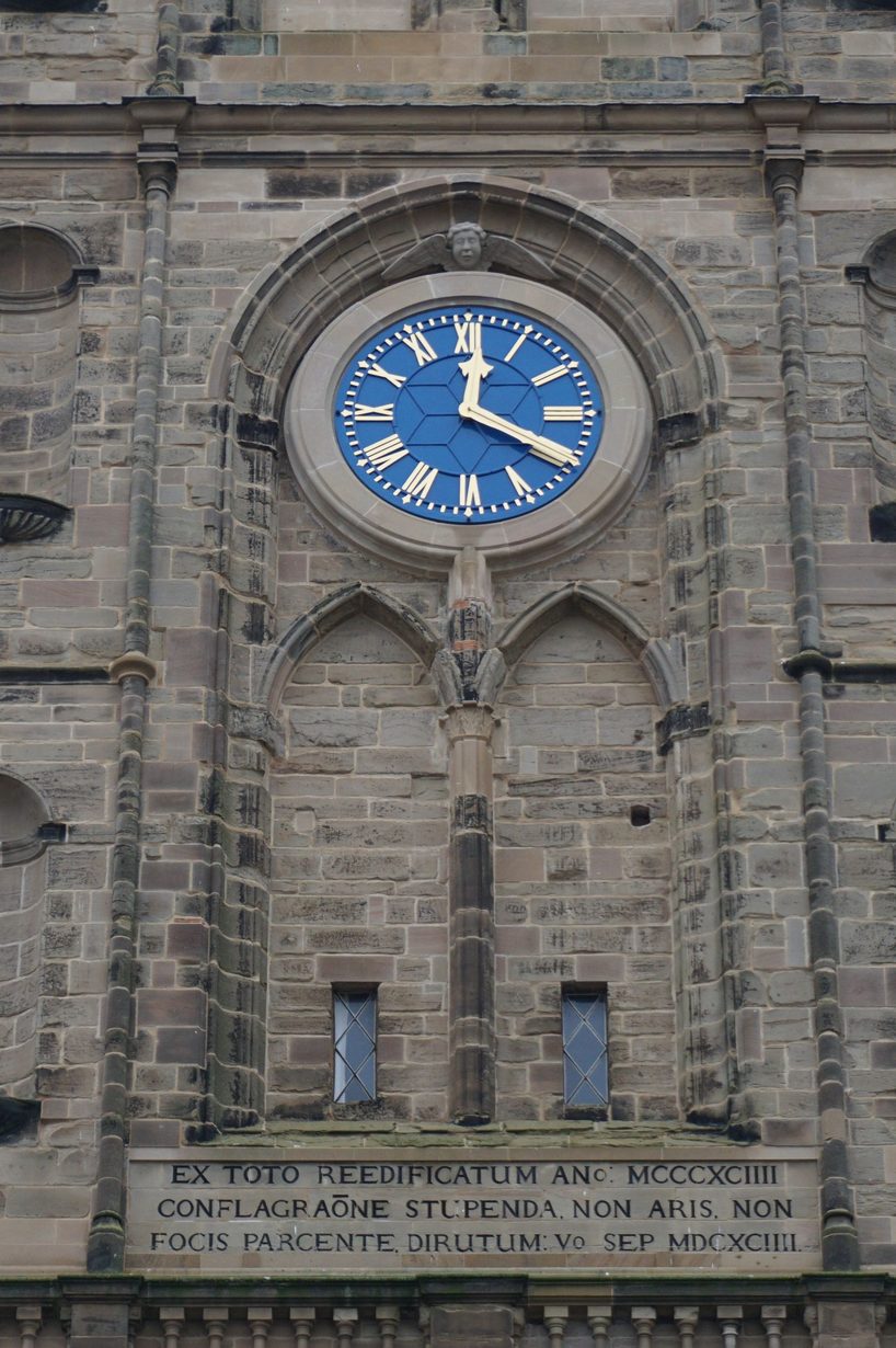 The blue clock face on the tower of St Mary's, Warwick, above a Latin inscription recording the fire of 1694