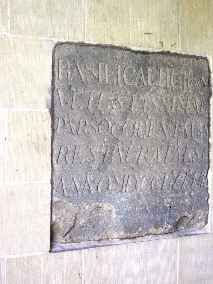 A square stone carved with Latin capitals recording the restoration of St Paul's Church, Jarrow, set in a plastered wall