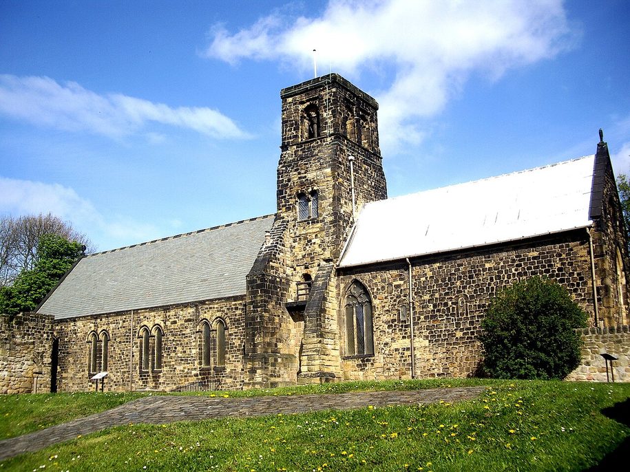 St Paul's Church, Jarrow, a low stone church with a tall narrow tower between its nave and chancel, seen across the grass
