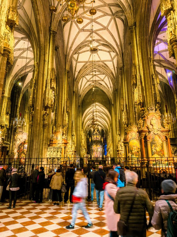 Visitors in the golden-lit Gothic nave of St Stephen's Cathedral, Vienna, looking towards the high altar