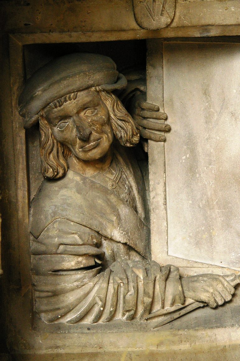 Carved stone bust of a man leaning out of a window opening beneath the stair of the pulpit in St Stephen's Cathedral