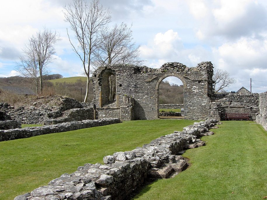 The low ruined walls and column bases of the abbey church at Strata Florida on a lawn, with the hills beyond