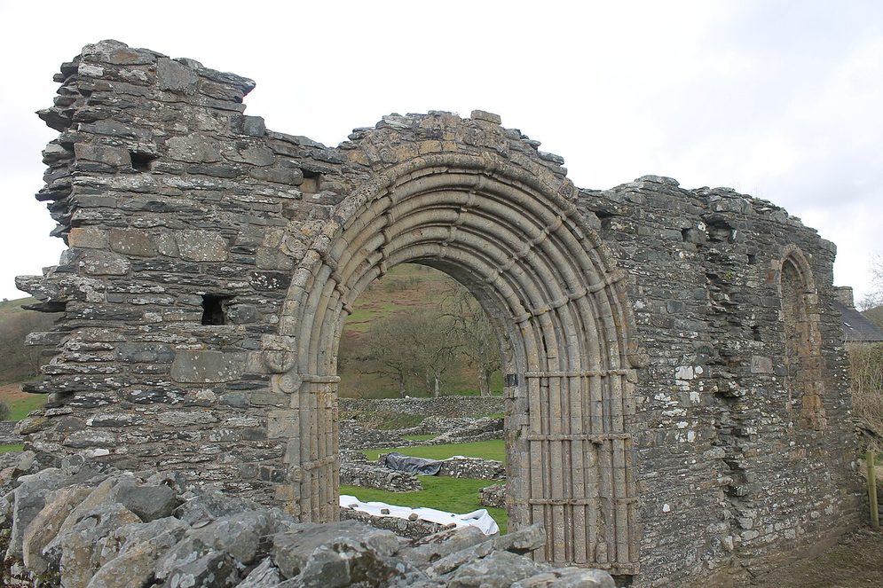 The round-arched west doorway of Strata Florida Abbey in its ruined stone wall, with lawn and low walls beyond