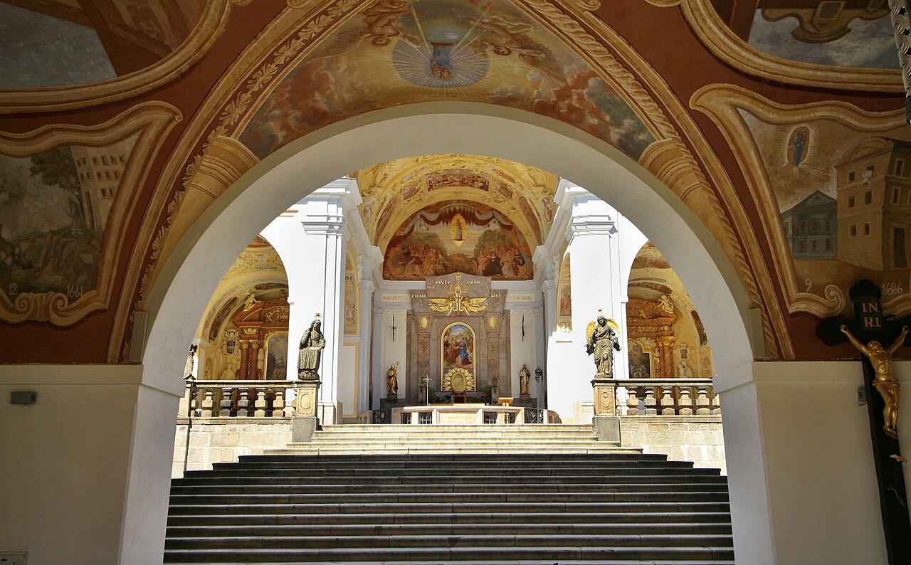 View through a painted arch of the cloister to the steps and altar of the Svatá Hora basilica