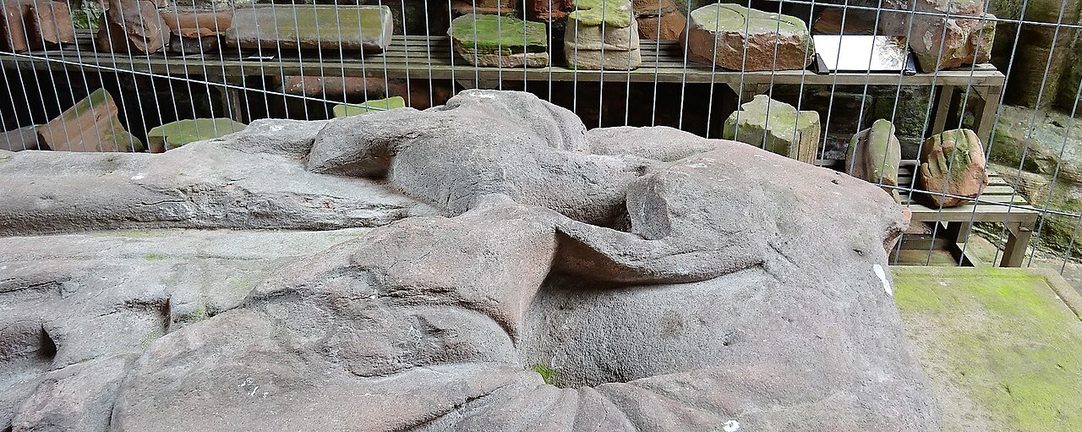 The worn stone effigy of Dervorguilla of Galloway lying in a tomb recess at Sweetheart Abbey, behind protective fencing