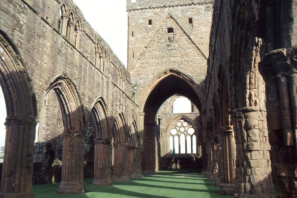 Looking east along the roofless nave of Sweetheart Abbey, between arcades of pointed red sandstone arches