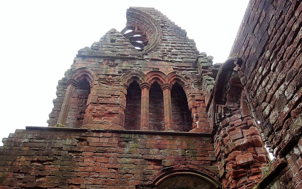The ruined red sandstone gable of the south transept of Sweetheart Abbey, with its windows and the circular window above
