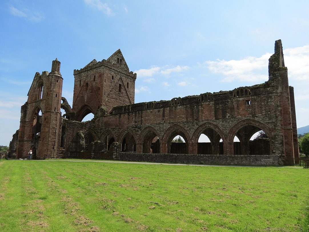 The red sandstone ruins of Sweetheart Abbey at New Abbey, its roofless church and central tower above the lawns