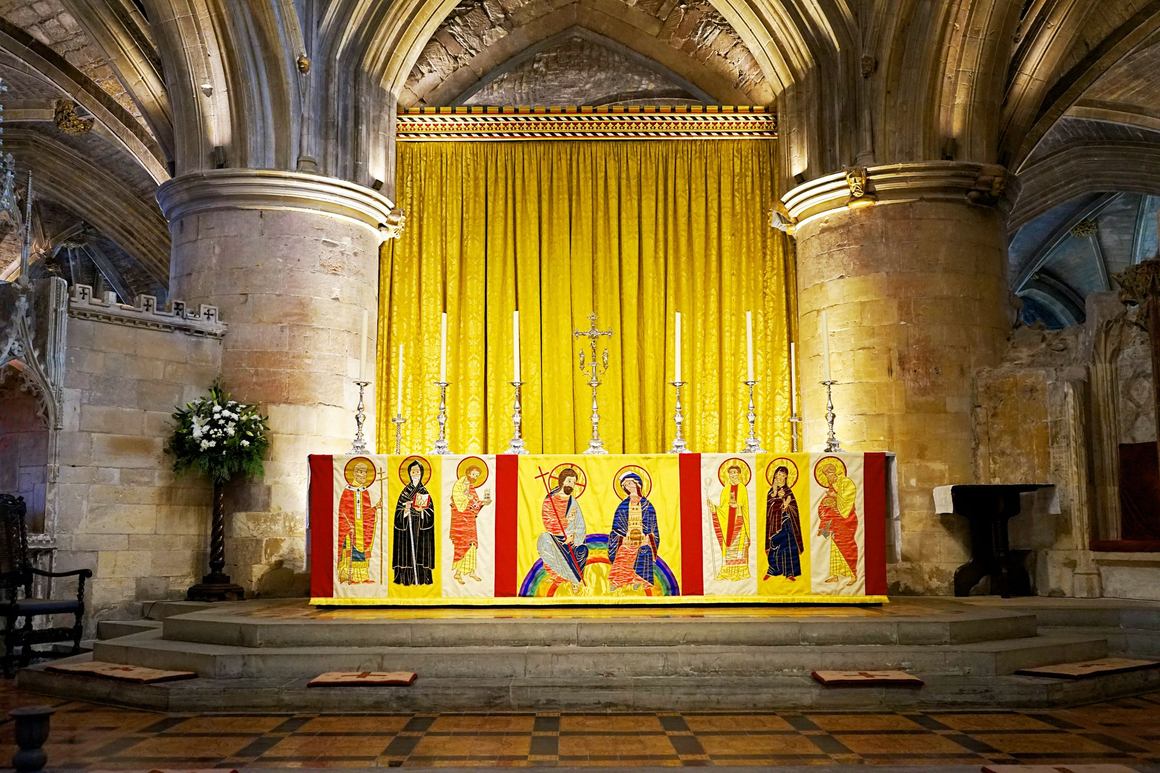 An ornate altar with a gold hanging and painted panels inside Tewkesbury Abbey