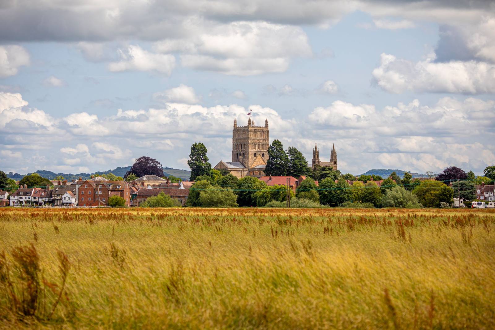 Tewkesbury Abbey's tower rising beyond a golden field outside the town