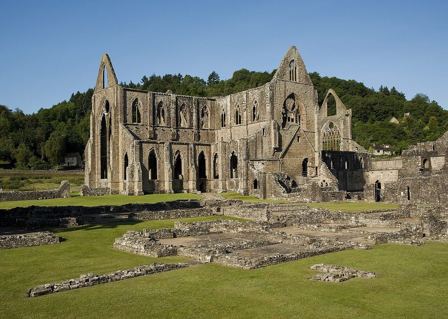 Low ruined walls of the cloister and monastic buildings at Tintern Abbey, with the church behind