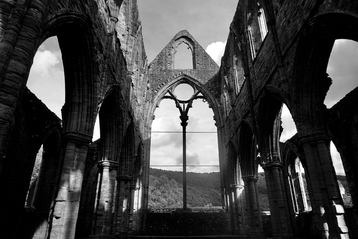 Black-and-white view inside the roofless nave of Tintern Abbey, looking through tall pointed arches to the empty east window