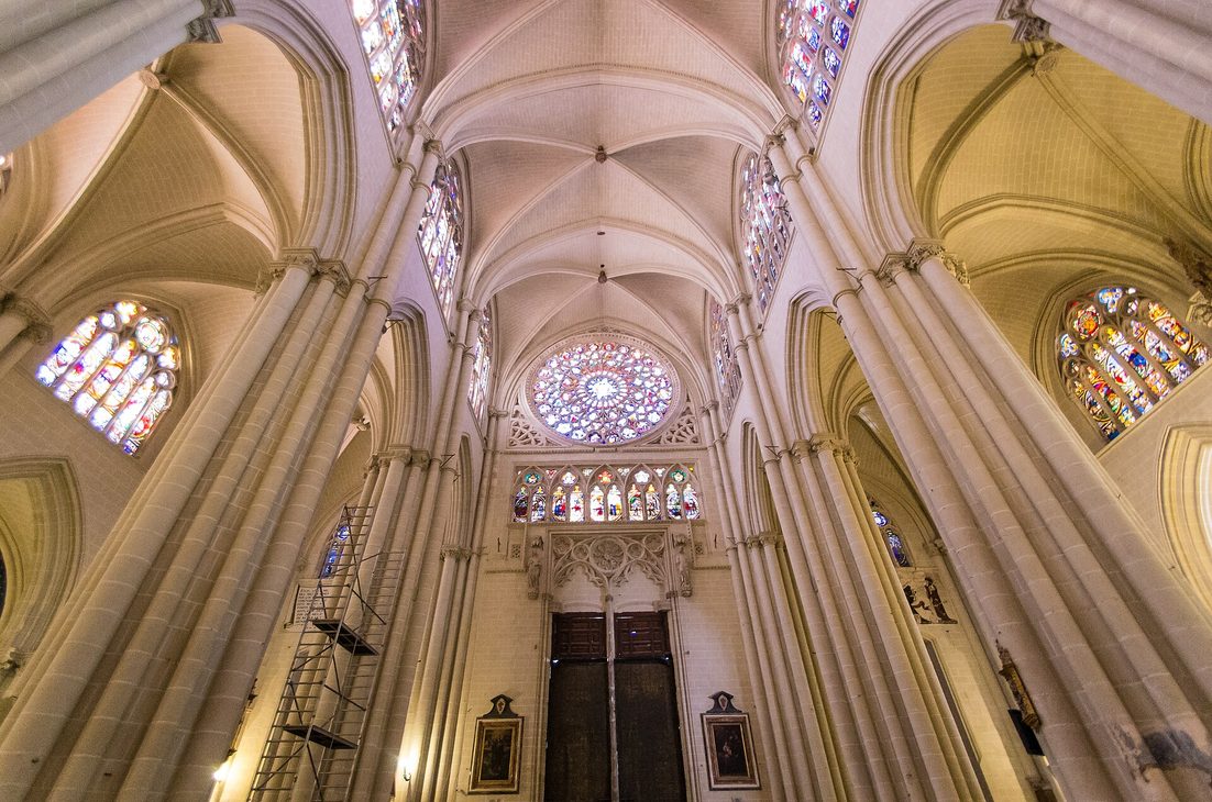 The pale soaring Gothic vaults and piers of Toledo Cathedral, with a rose window at the end