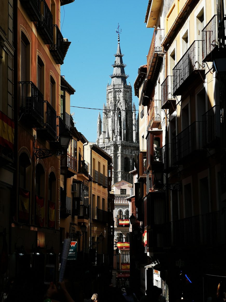 The Gothic spire of Toledo Cathedral seen at the end of a narrow street of tall houses