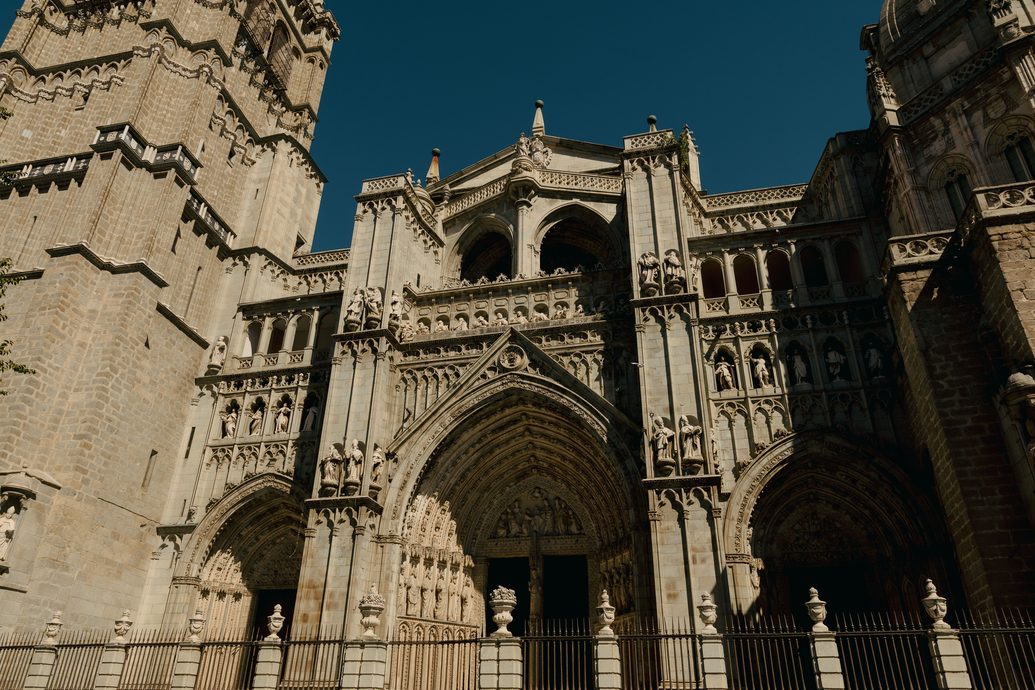 The Gothic west front of Toledo Cathedral, with its carved portals and tower, under a deep blue sky