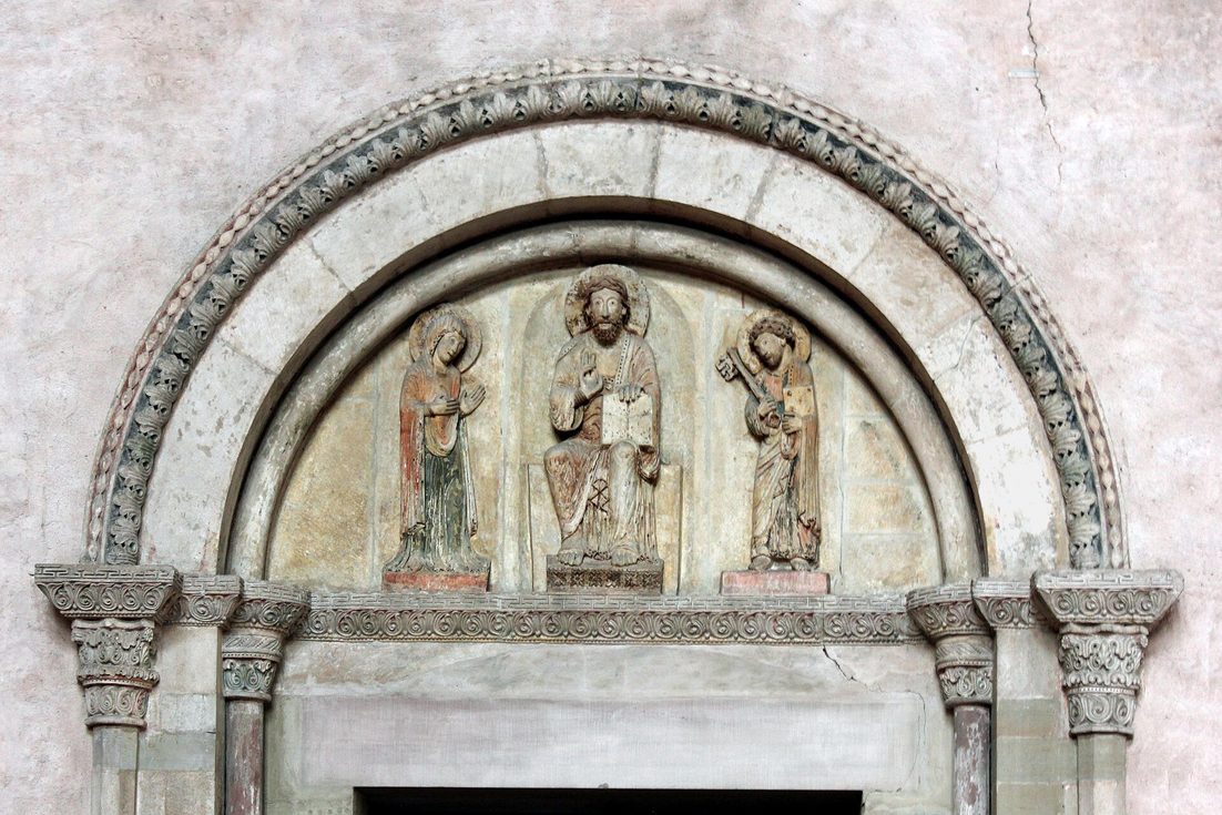 A painted Romanesque tympanum showing Christ enthroned between the Virgin Mary and St Peter, over a doorway in Trier Cathedral