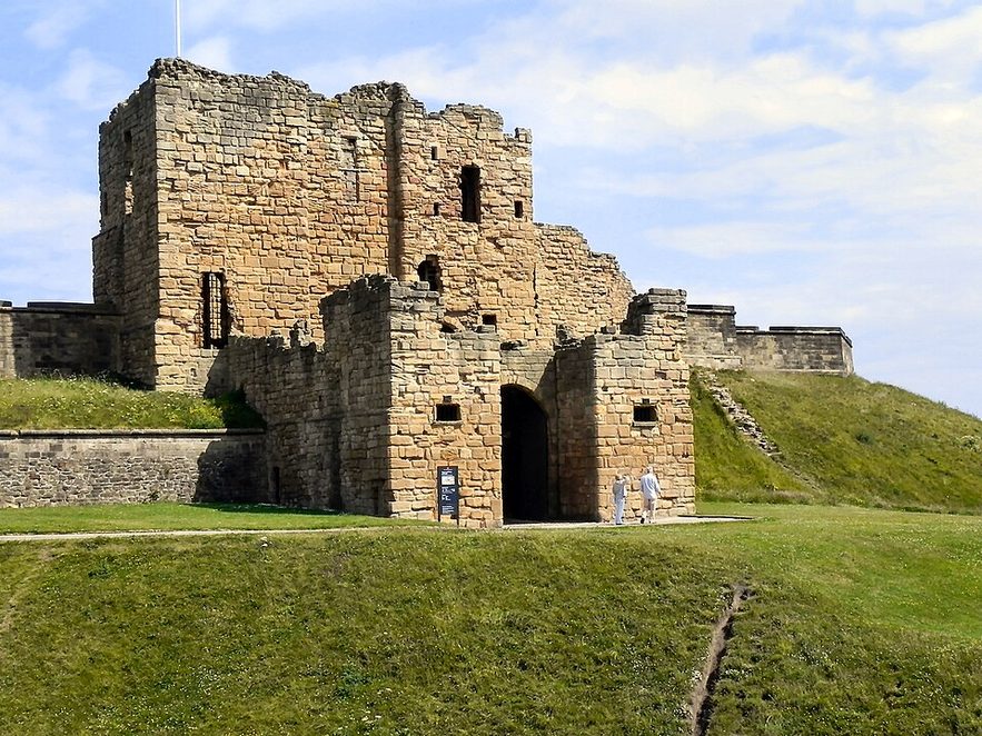 The stone gatehouse of Tynemouth Castle, a tall square tower with an arched entrance, on a grassy slope