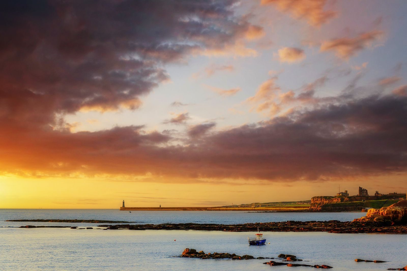 Sunset over the sea at Tynemouth, with the priory ruins and the pier lighthouse on the headland in the distance