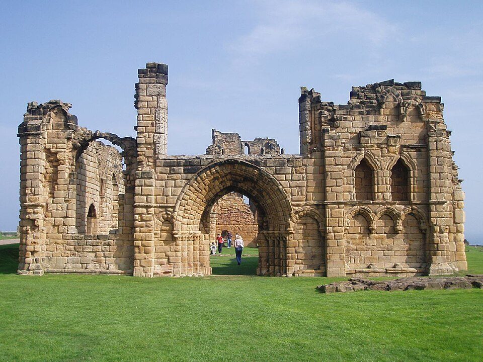 The ruined round-arched west doorway and walls of the nave at Tynemouth Priory on a grassy headland