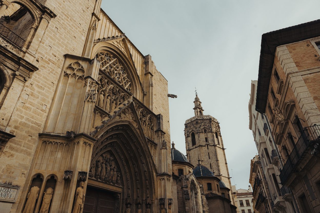 The Gothic Apostles' Door of Valencia Cathedral with its rose window, and the octagonal Micalet bell tower behind, seen from a narrow street