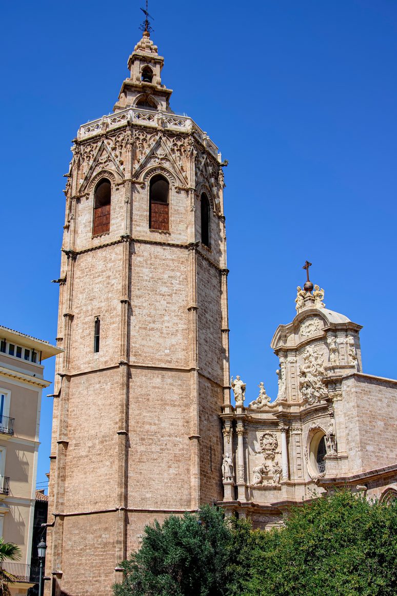 The tall octagonal Micalet bell tower of Valencia Cathedral beside the Baroque Door of the Irons, under a deep blue sky