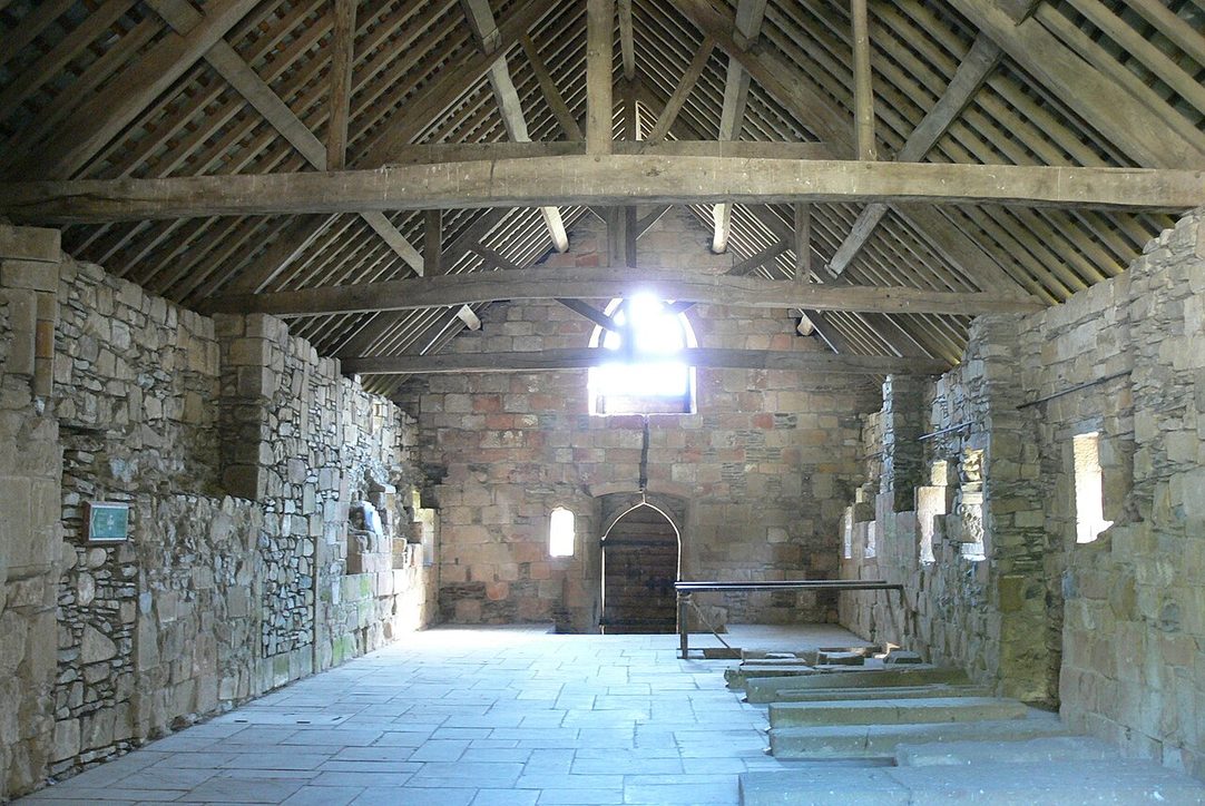 The long monks' dormitory at Valle Crucis Abbey under its timber roof, with carved grave slabs along the walls