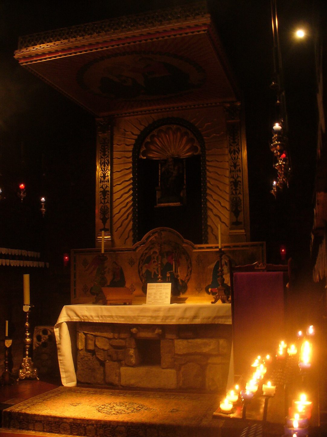 Inside the Holy House at the Anglican shrine in Walsingham, a small dark chapel lit by candles around the altar