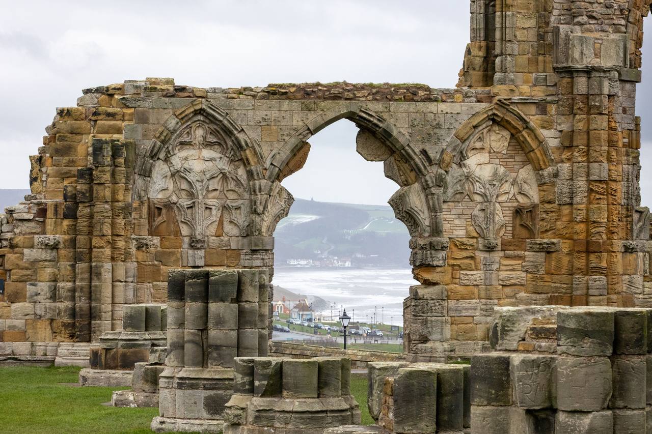 A ruined arch of Whitby Abbey framing a view of the town and harbour below