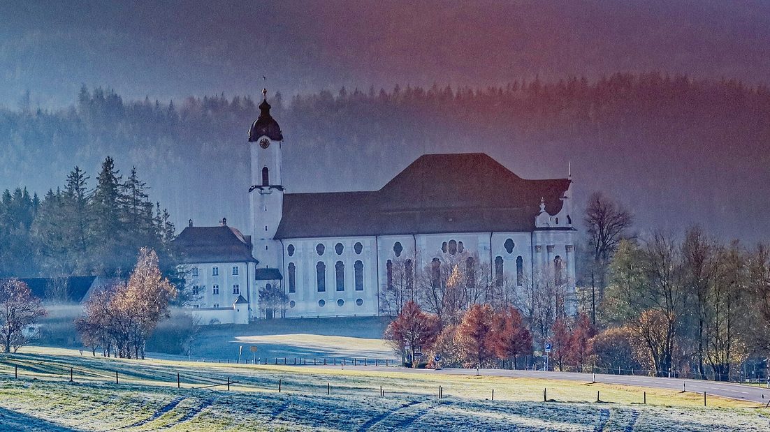 The Wieskirche on a frosty morning, white walls and red roof among bare trees and frosted meadows