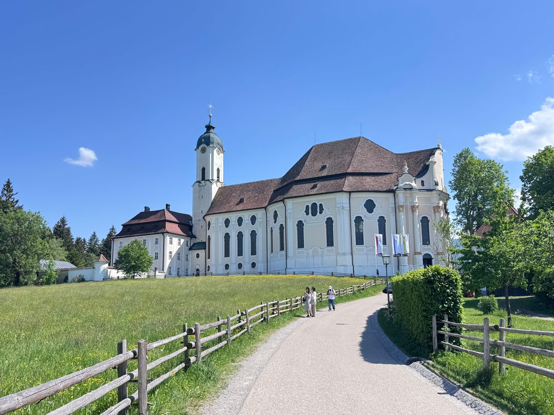 The white Wieskirche with its red roof and bell tower at the end of a path through green meadows under a blue sky