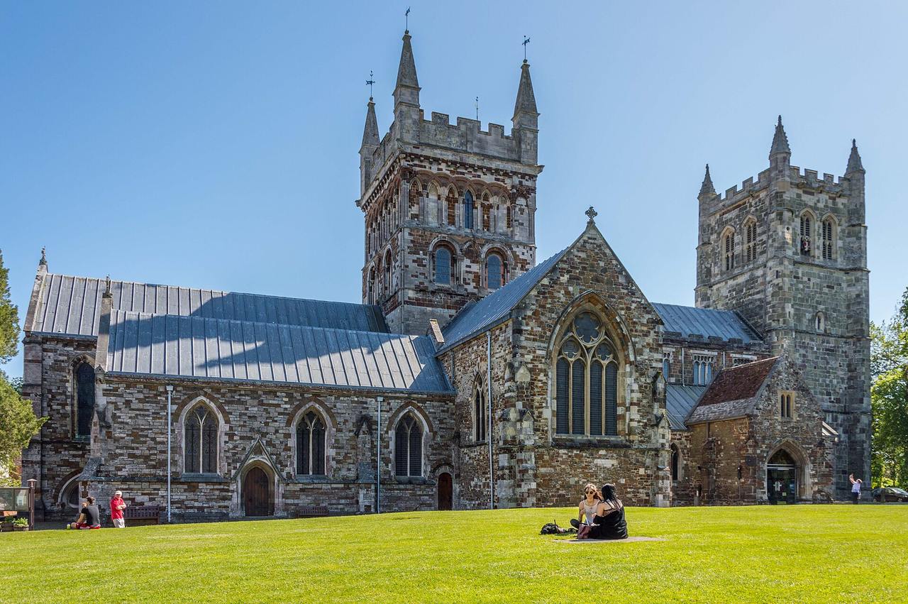 Wimborne Minster with its two towers of chequered stone seen across the green on a sunny day