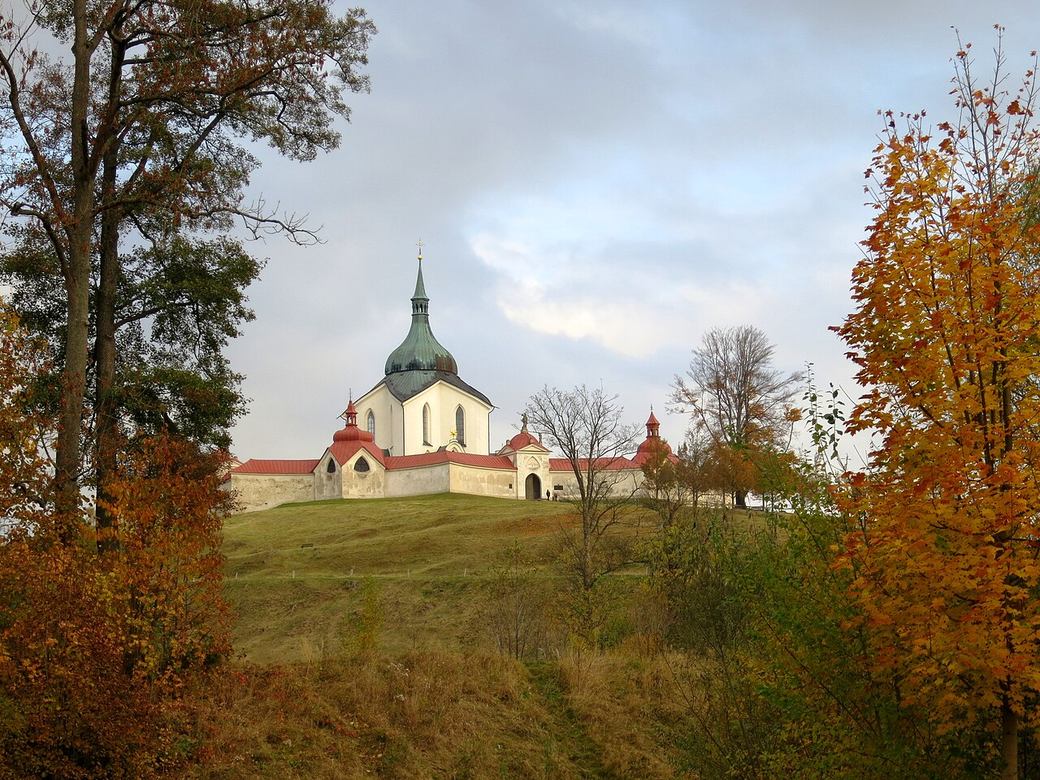 Zelená Hora church seen across a grassy slope framed by autumn trees
