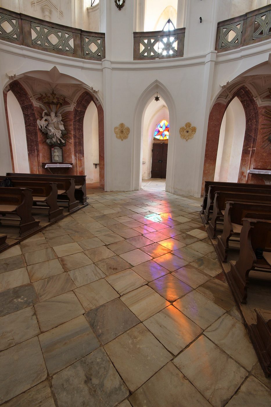 The pale interior of Zelená Hora church with pointed arches and coloured light on the floor
