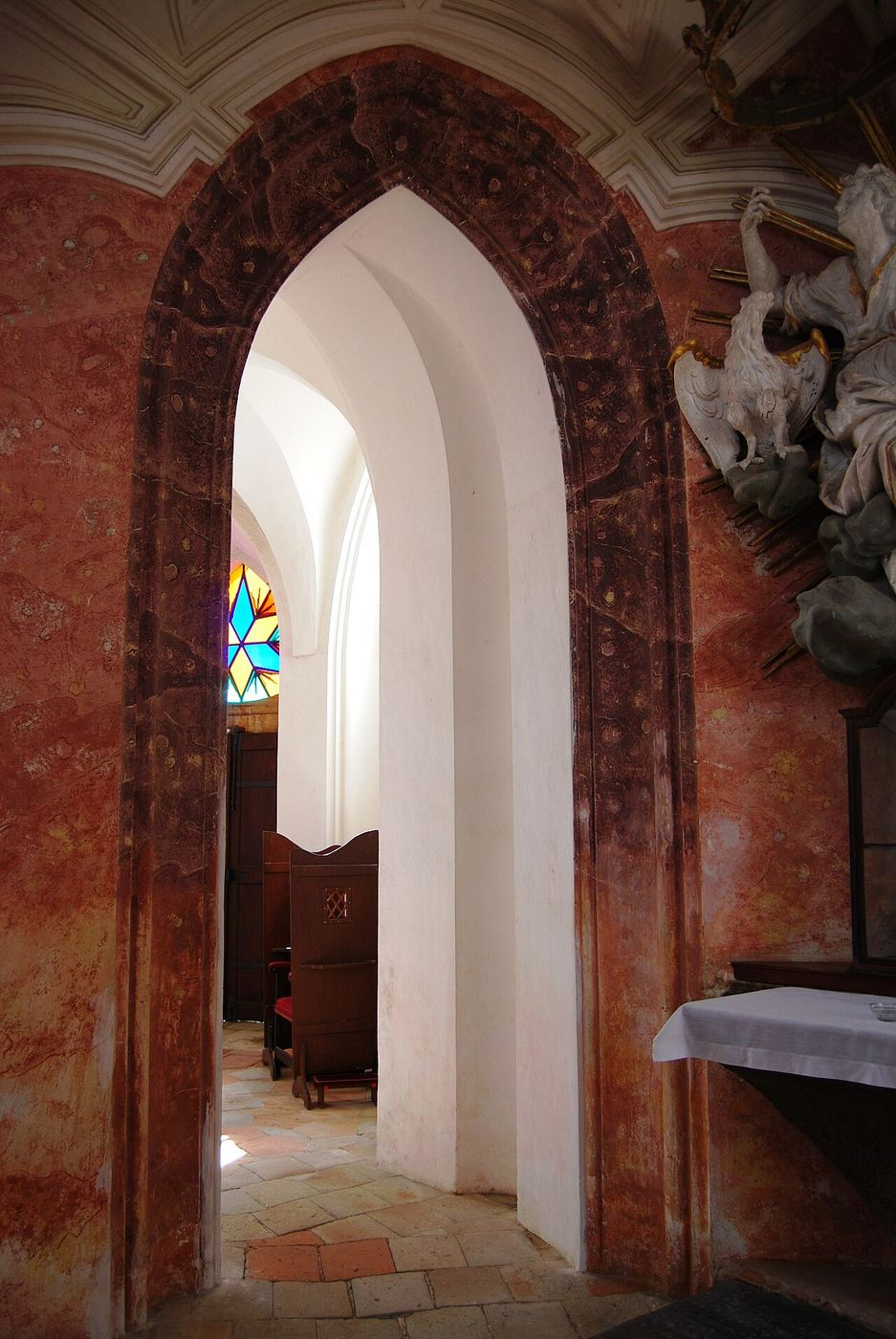 A pointed arch opening into a side chapel with red marbled walls in Zelená Hora church