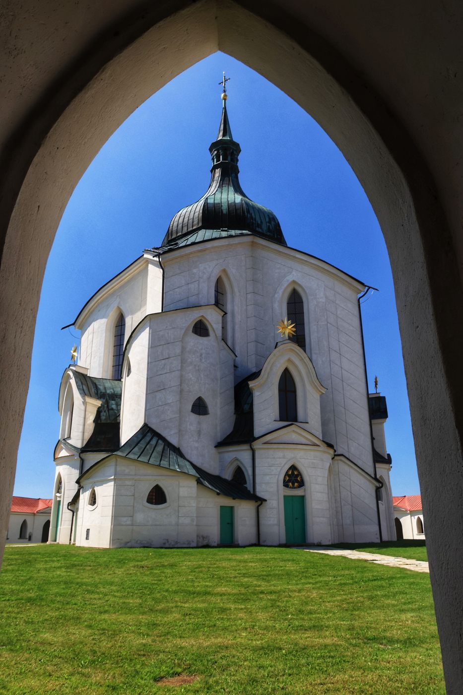 The Zelená Hora church framed by a pointed arch of the cloister gate against a blue sky